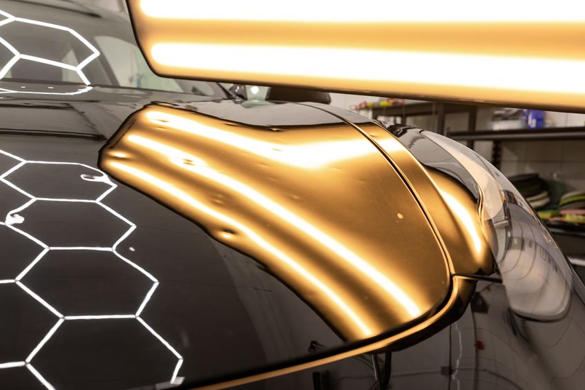 Hood of black car with reflective light overhead.